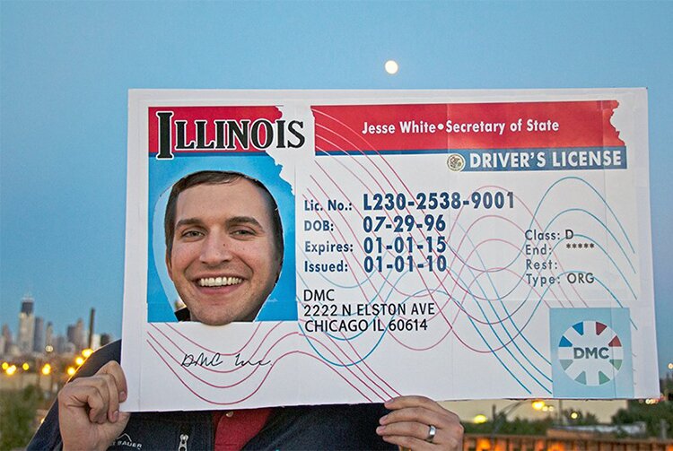 Photo of Eric West posing with his face inside a giant fake DMC Illinois Drivers License. 