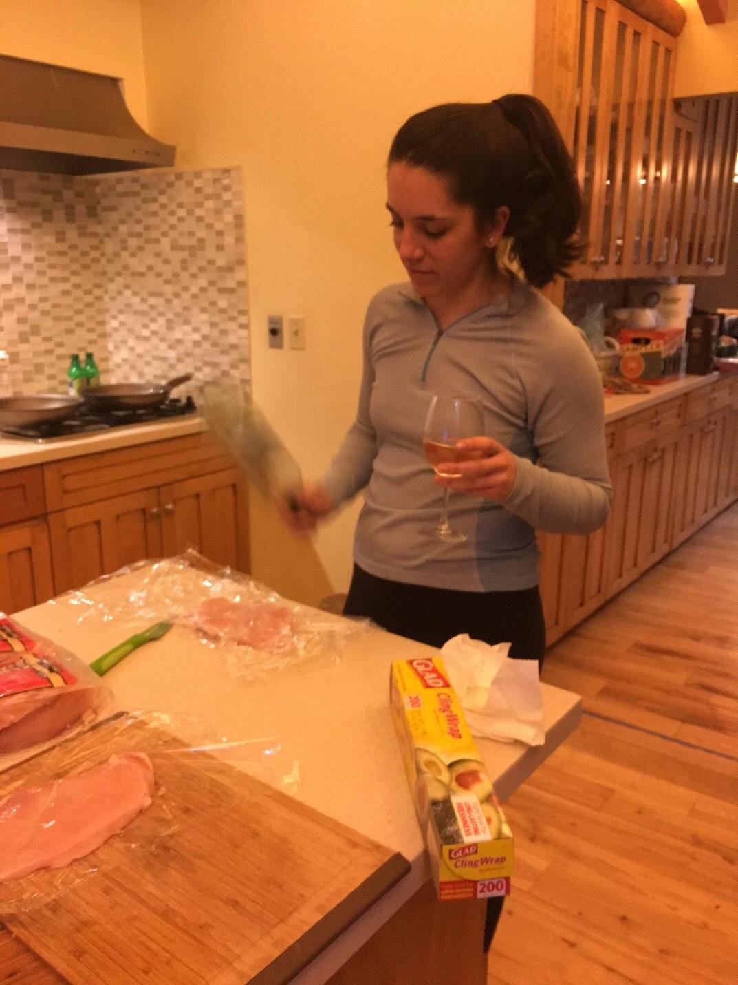 Photo of Emily using a wine bottle to flatten chicken breasts.