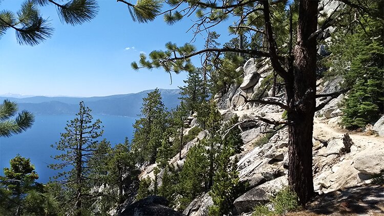 Photo from  the trail overlooking Lake Tahoe far below with Sierra Nevada mountains in the background.