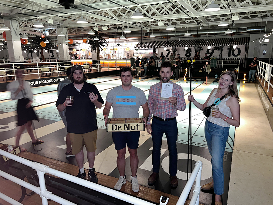 Four people stand at a shuffleboard venue