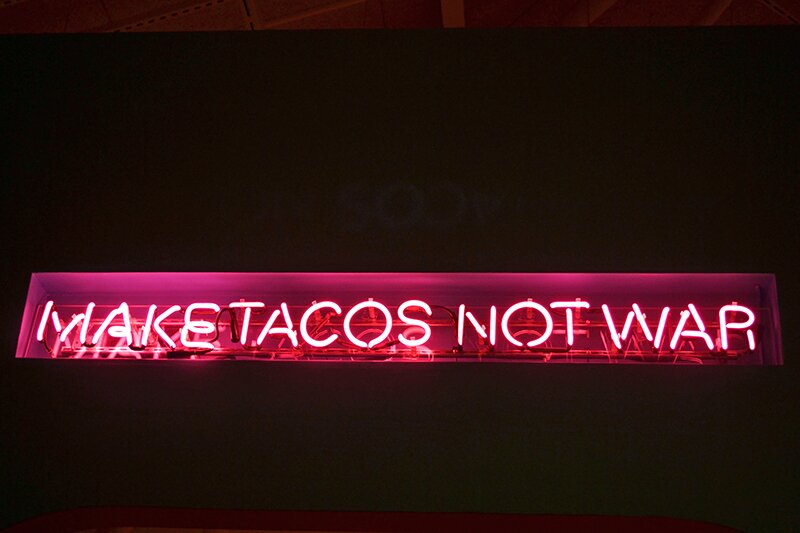 Neon sign reading "Make Tacos Not War"