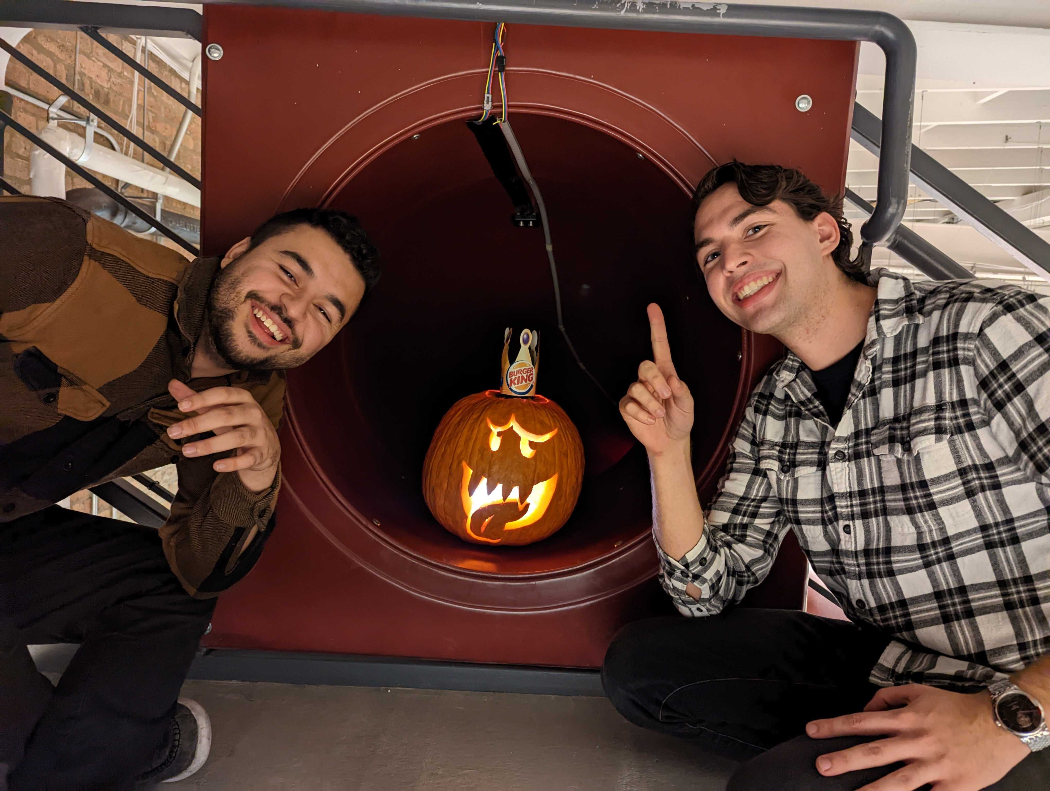 Two people pose by a carved jack-o-lantern