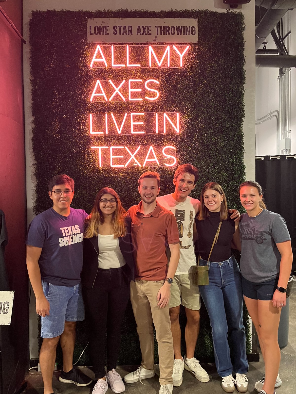A group of people in front of a neon sign reading "All my axes live in Texas"